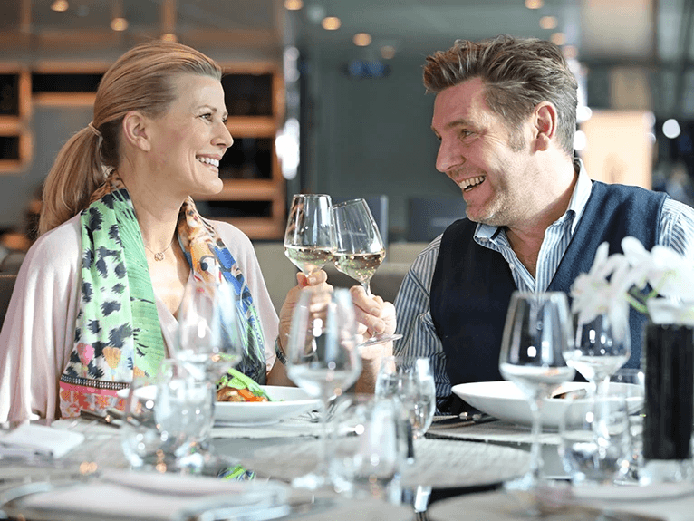 A man and woman toasting with a glass of wine at Crystal Dining on a Scenic river cruise ship. 