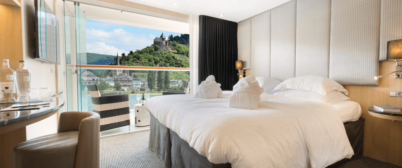 Queen bed next to the Scenic Sun Lounge in the Standard Balcony Suite, with an open window showing the passing landscapes.