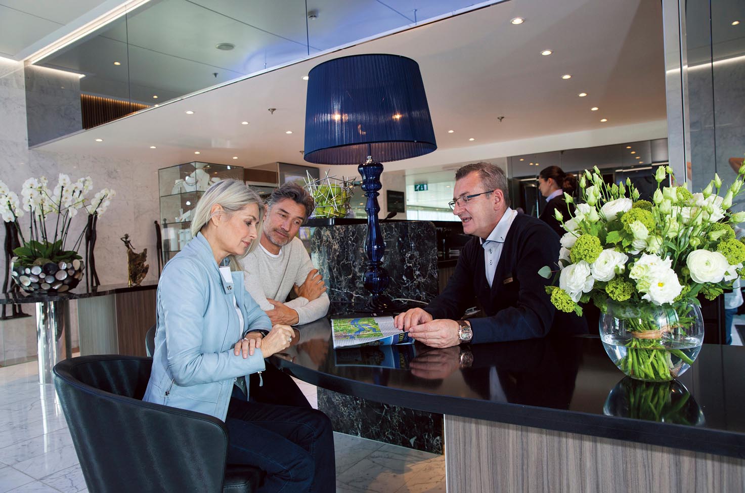 Guests speaking to Cruise Director on board Scenic Diamond in the reception area. 