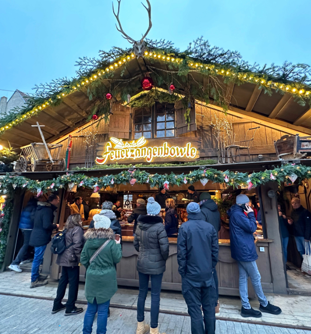 A festive gathering of people enjoying a charming Christmas market adorned with twinkling lights and seasonal decorations.