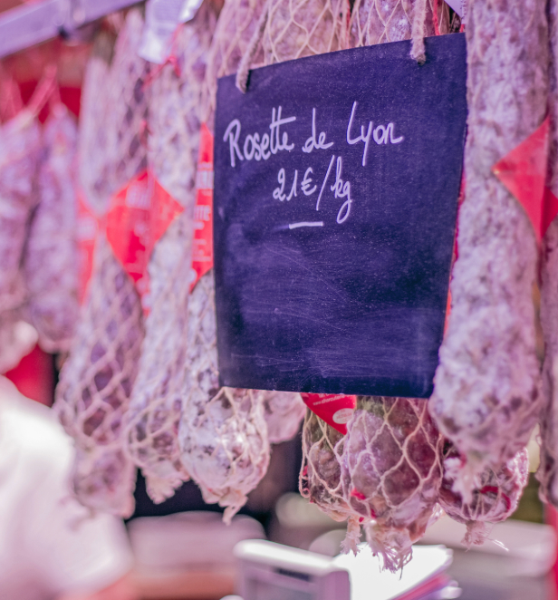 A display of hanging meats in a butchers with a slate showing the price. 