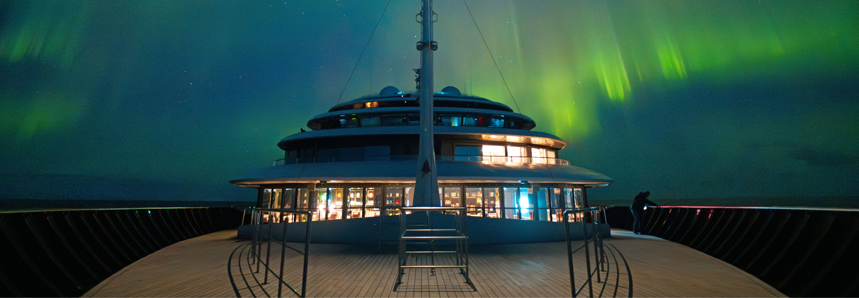 The deck of a boat offers a stunning view of the aurora borealis lighting up the night sky above.