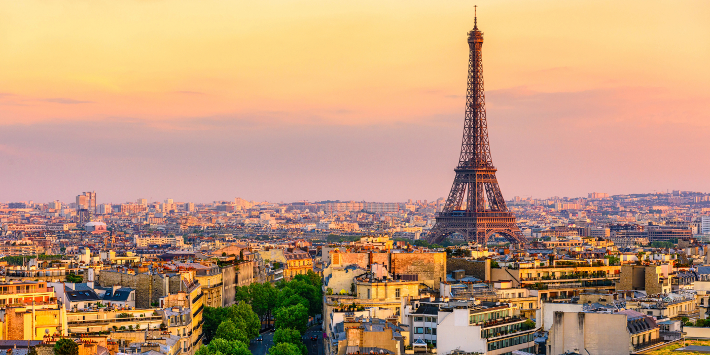 The Eifel Tower can be seen on a beatiful evening in Paris. The orange sky bathes the city below in yellow light.