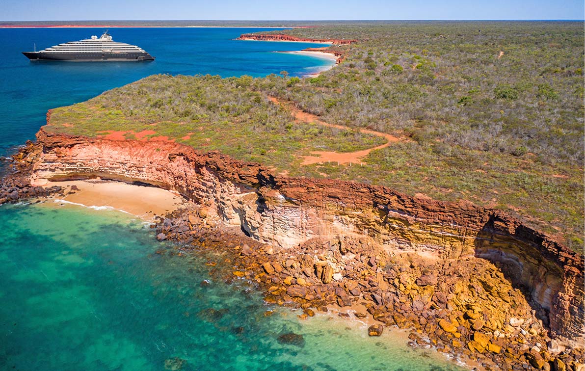 Scenic Eclipse Yacht off the coast of Broome with orange rocky coastline and clear blue water