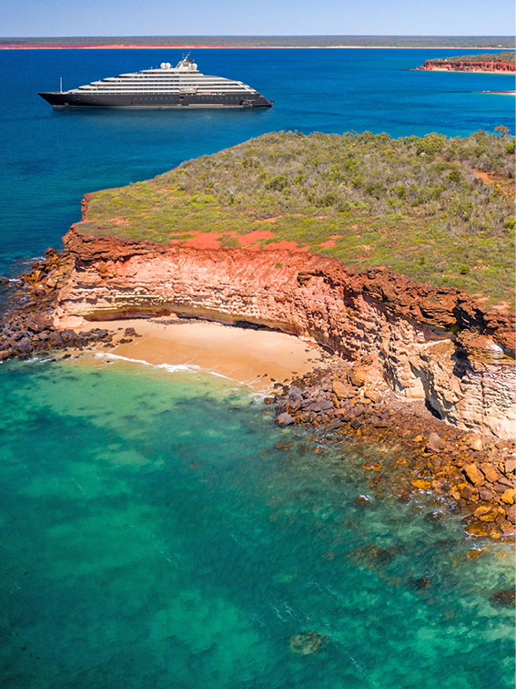 Scenic Eclipse Yacht off the coast of Broome with orange rocky coastline and clear blue water