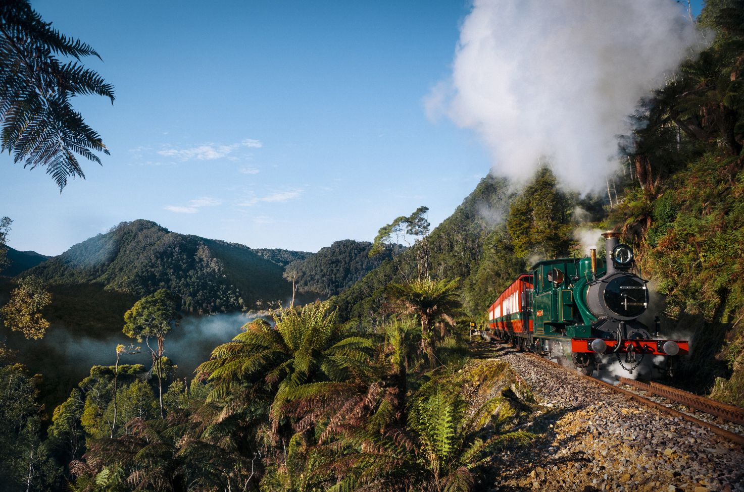 Train puffing steam on the ridge of a mountainside with lush greenery surrounding the terrain