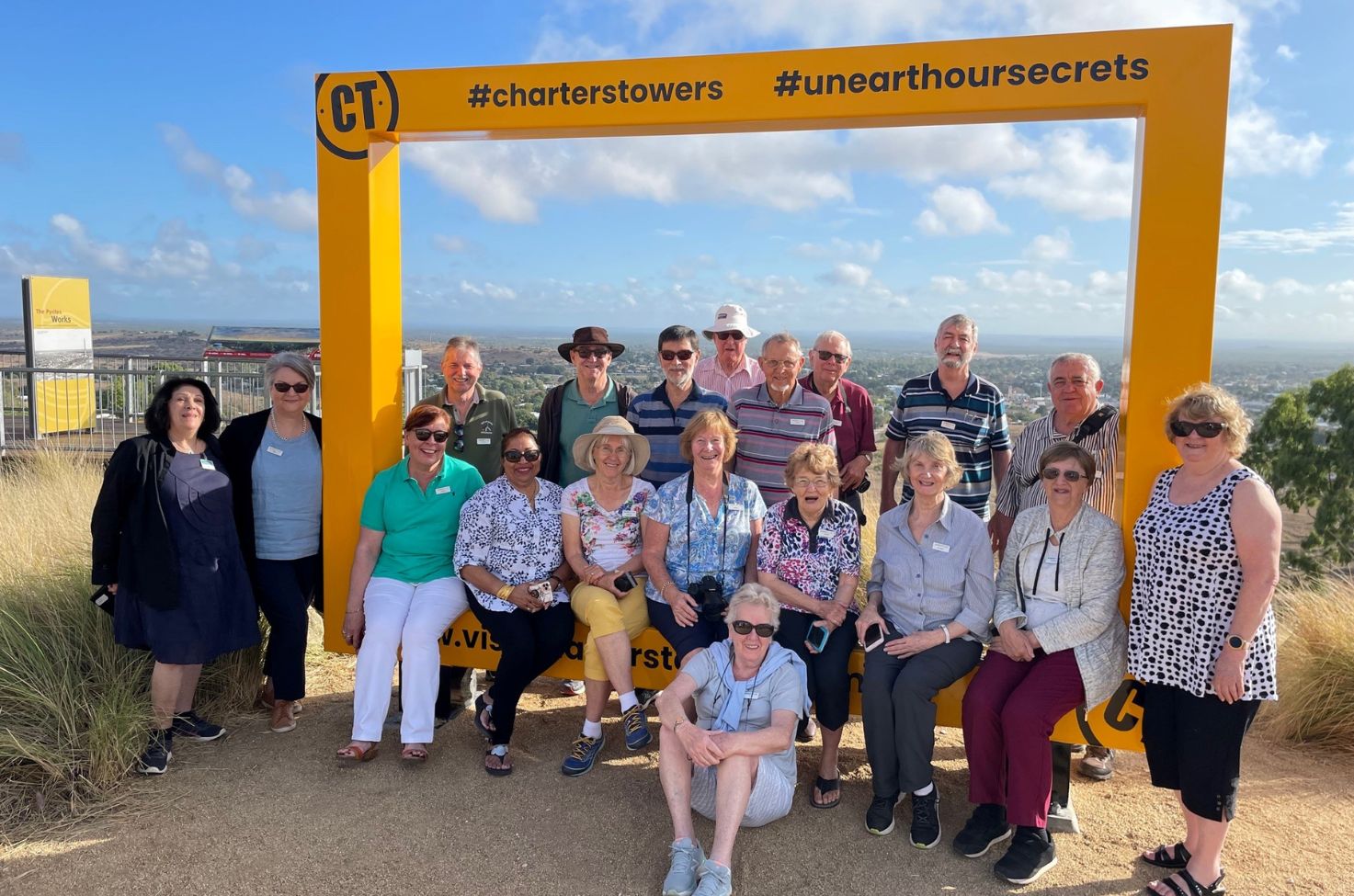 Group of people on a tour posing under a yellow sign in Outback Queensland, Australia