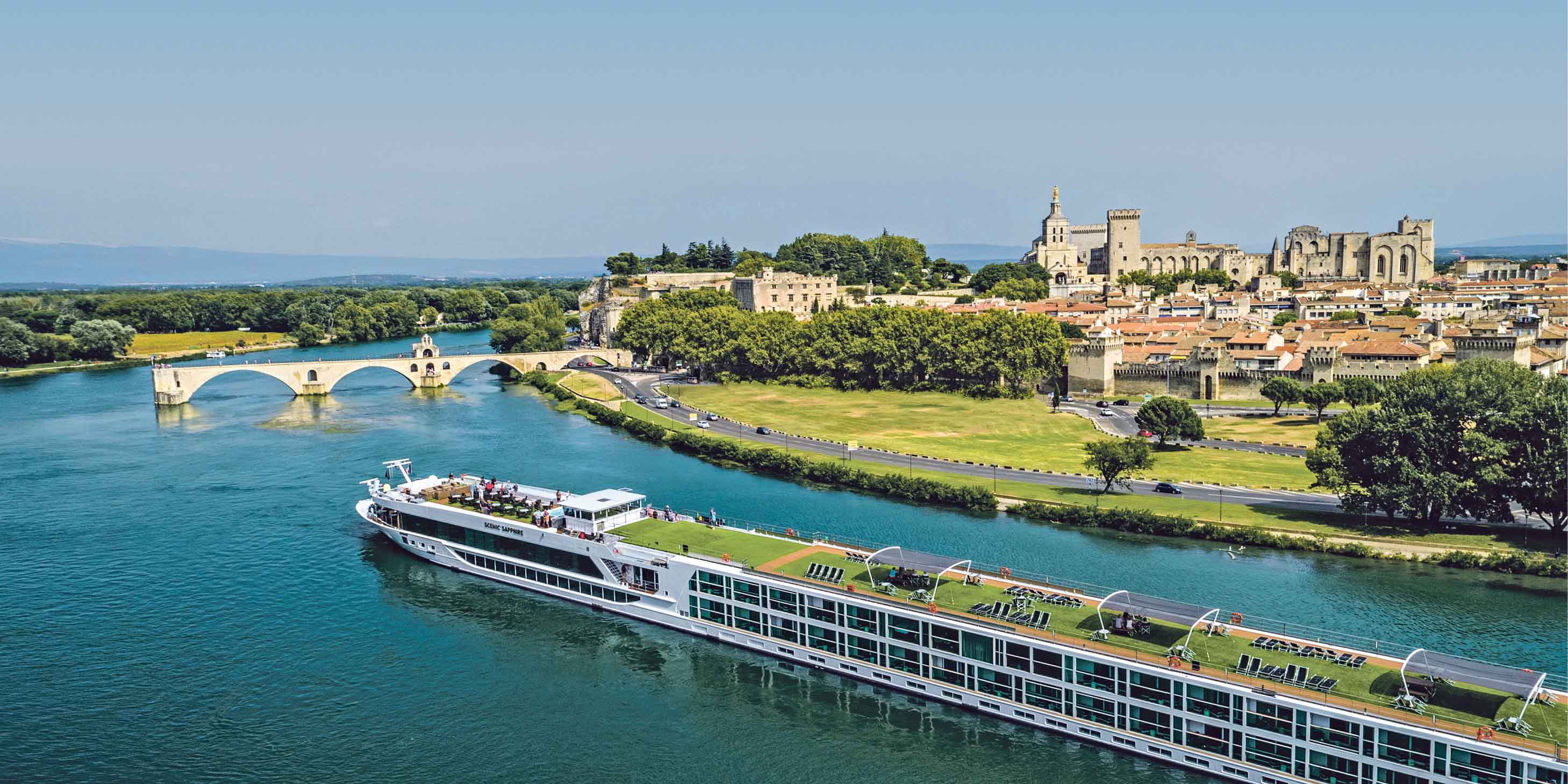 River cruise ship sailing past the Saint Bénézet stone bridge ahead and Avignon to the right