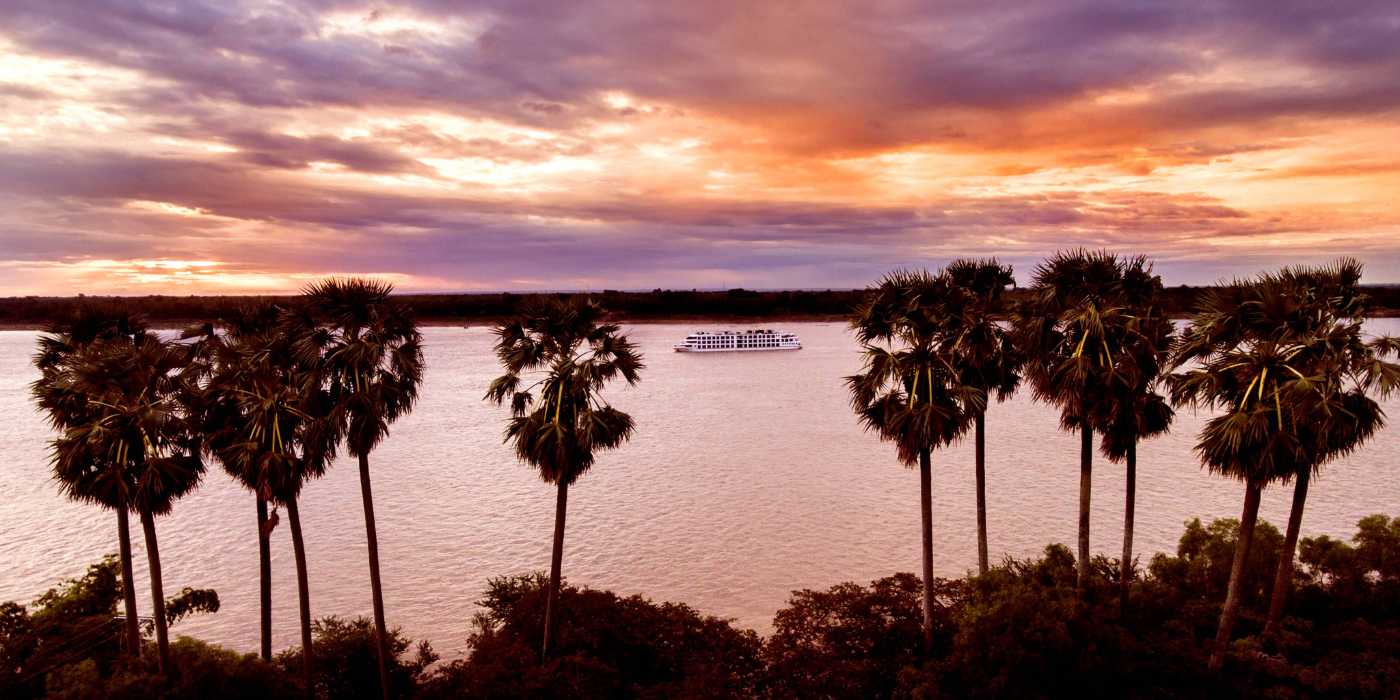 A river ship cruising the Mekong in the sunset with palm trees in the foreground