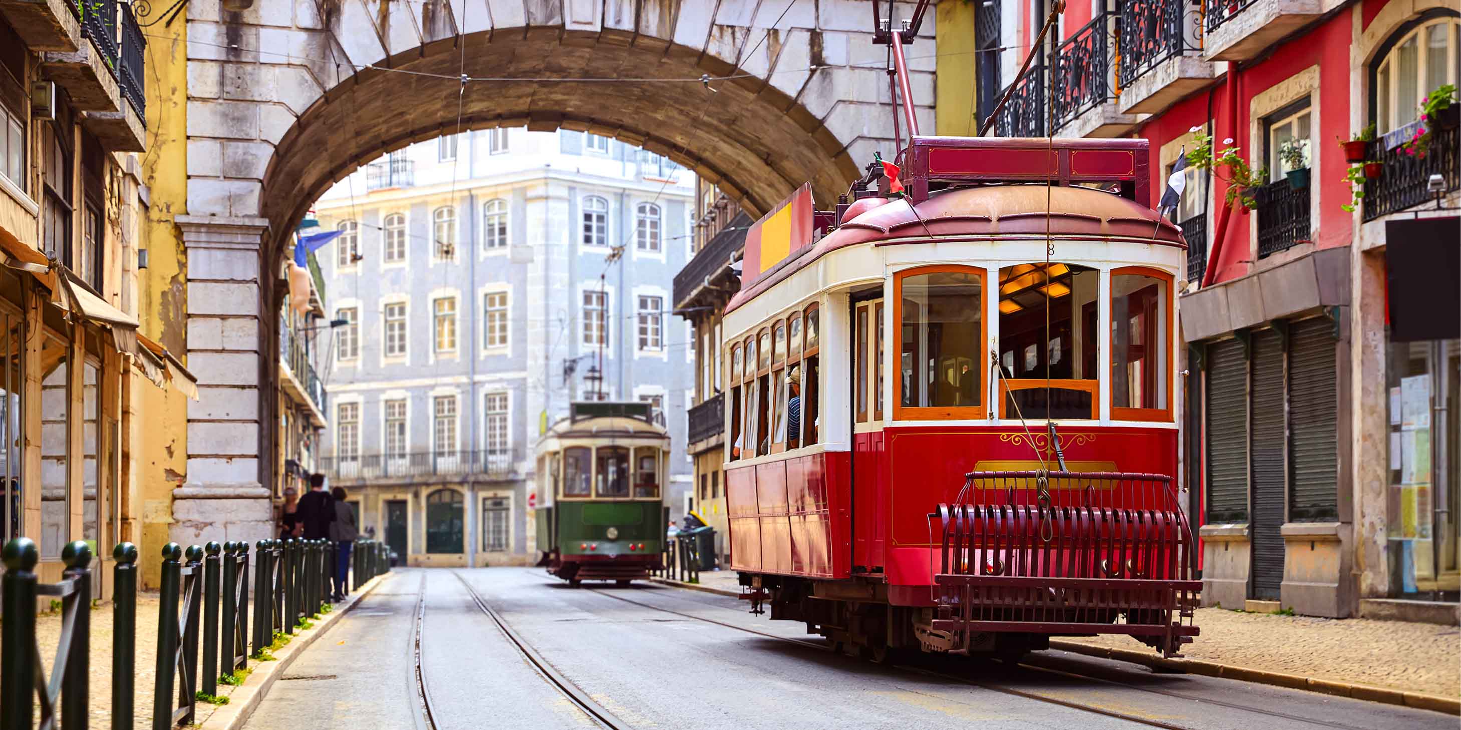 Red and green trams travelling past colourful buildings in Lisbon, Portugal.