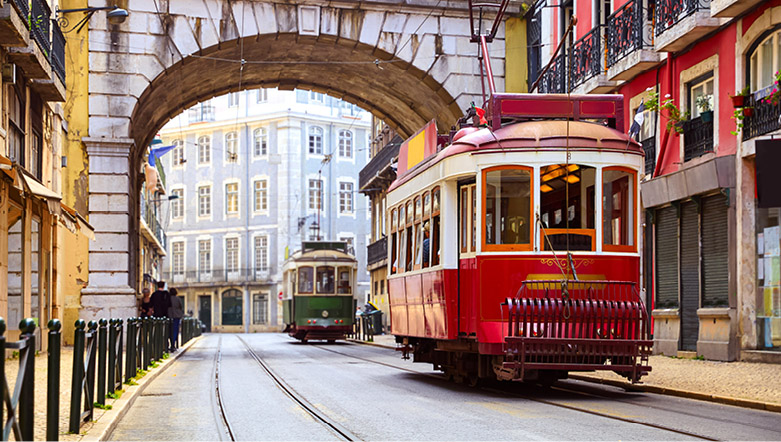 Red and green trams travelling past colourful buildings in Lisbon, Portugal.