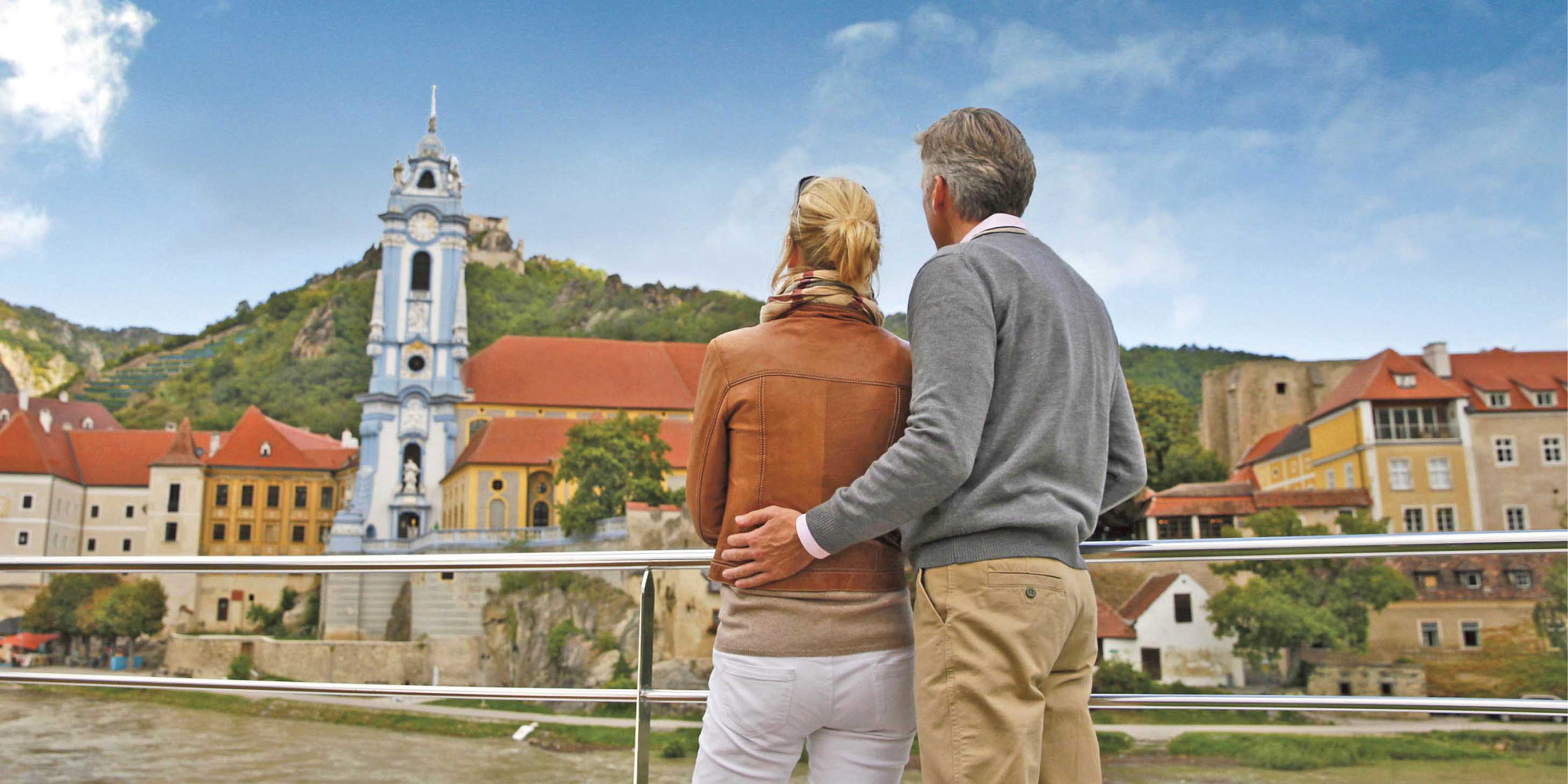 A couple stand on the sun deck of a Scenic Space-Ship admirning the buildings and scenery of Durnstein, Austria