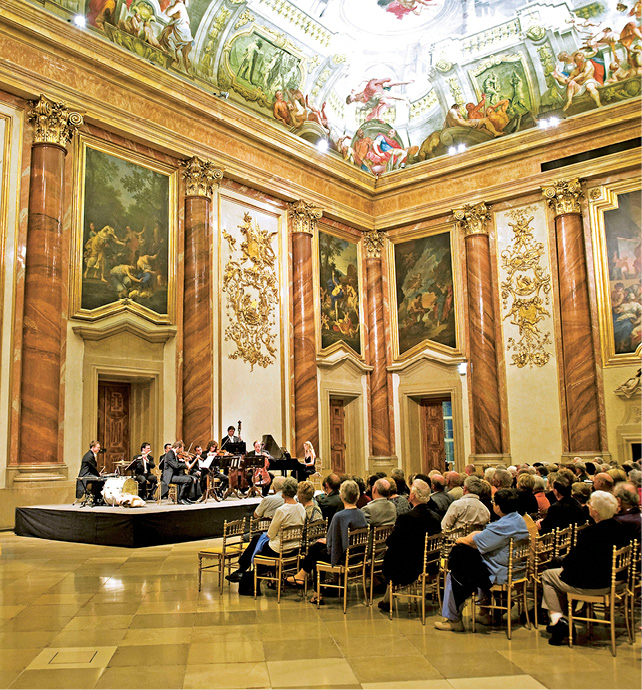 A classical concert in the opulent interiors of Palais Liechtenstein with classical paintings, gold detailing, and wooden columns 