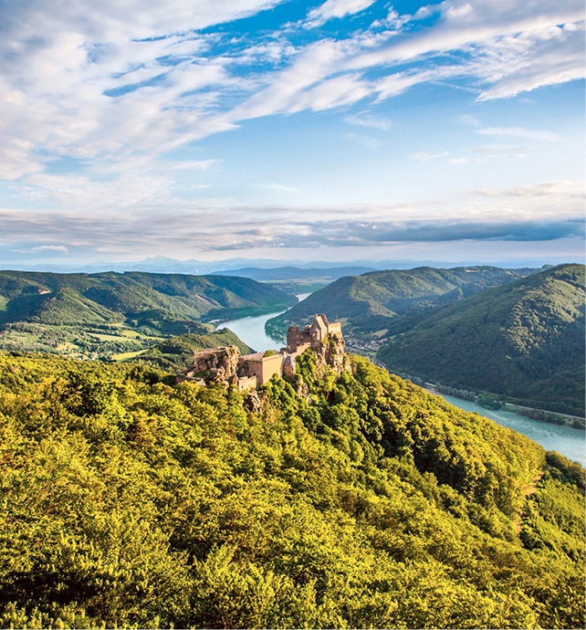a Scenic river ship cruises through the green hills of the Wachau valley with an old castle perched on the hilltop 