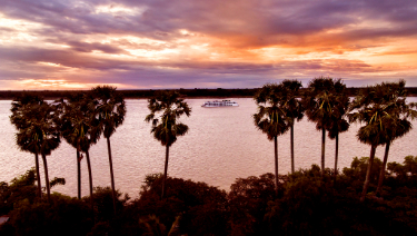 Scenic Spirit can be seen sailing along the Mekong. The sun can be seen setting in the background