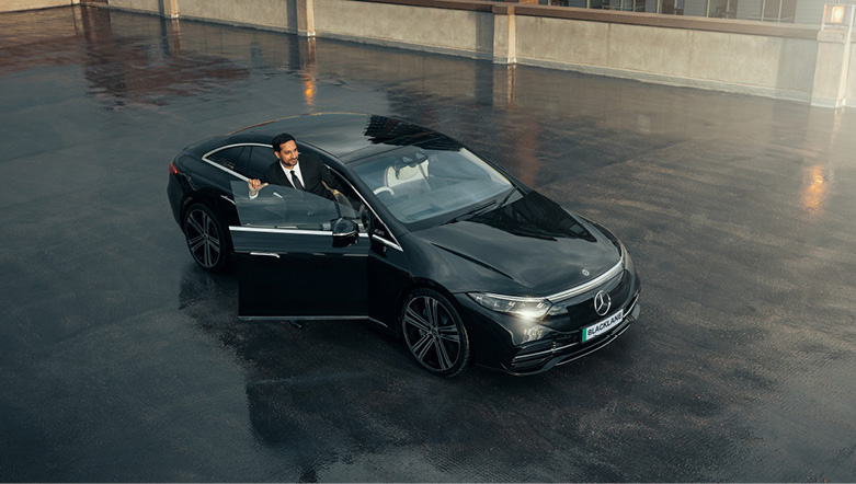 Chauffeur driver wearing a suit stepping out of the door of a luxury black vehicle