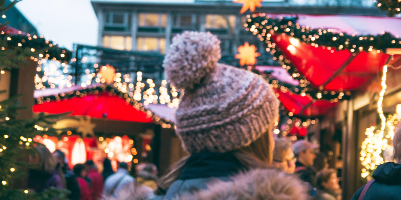 Woman walking through bustling market with Christmas lights.
