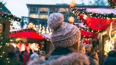 Woman walking through bustling market with Christmas lights.