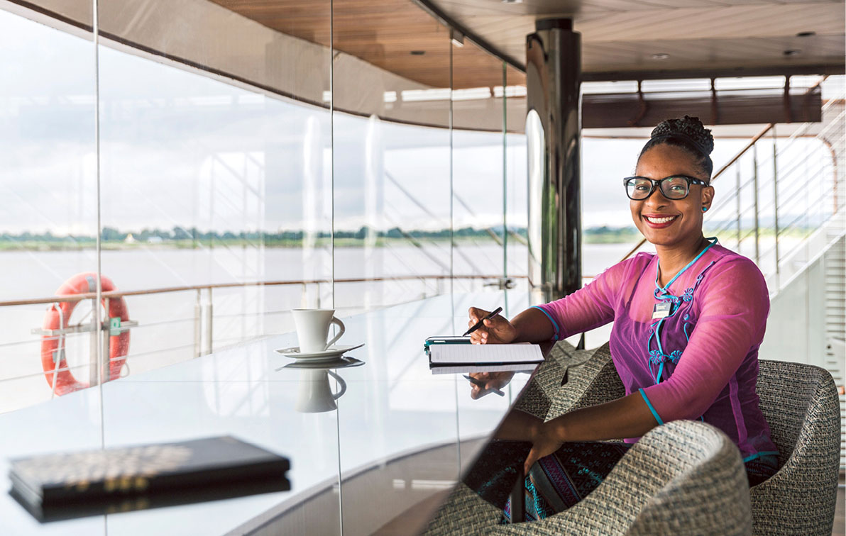 Women sitting at a desk with floor to ceiling views whilst sailing the Mekong