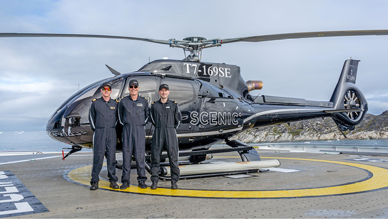 Helicopter crew standing in front of helicopter on landing pad