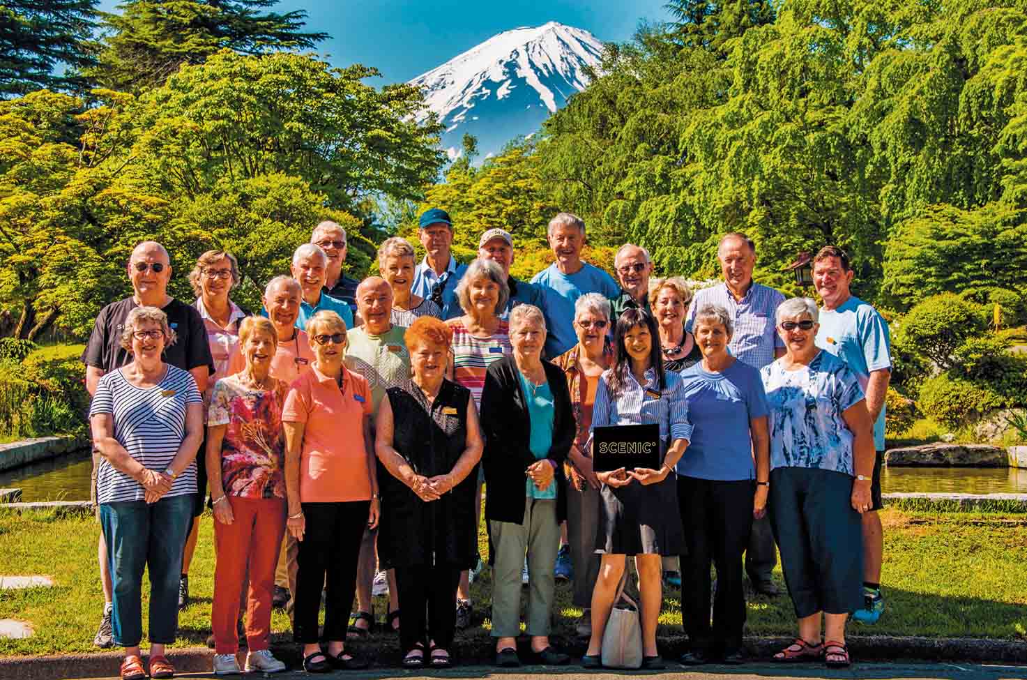 Group of travellers posing for a photo with Mount Fuji peeking through the ridgeline of the trees in the background
